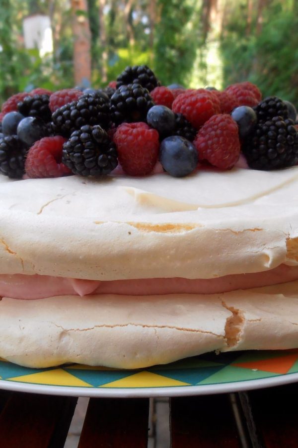 An image of Meringue Torte seen from the side. There are different types of berries on top of the meringue cake.
